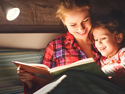 Woman and child reading a book in bed with a light