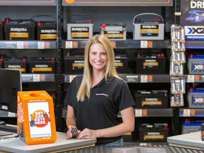Batteries Plus employee standing next to a Get Car Keys Here sign