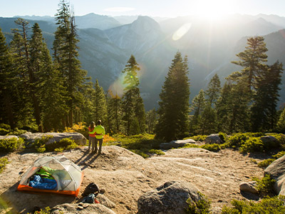 People standing at a rock edge overlooking a forest with tent behind them