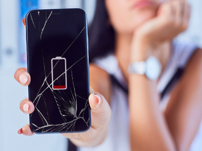 person holding out a phone with a broken screen and dead battery