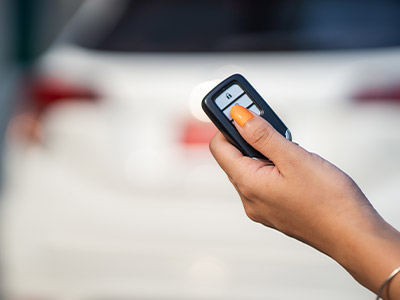 Person clicking a key fob behind a white vehicle